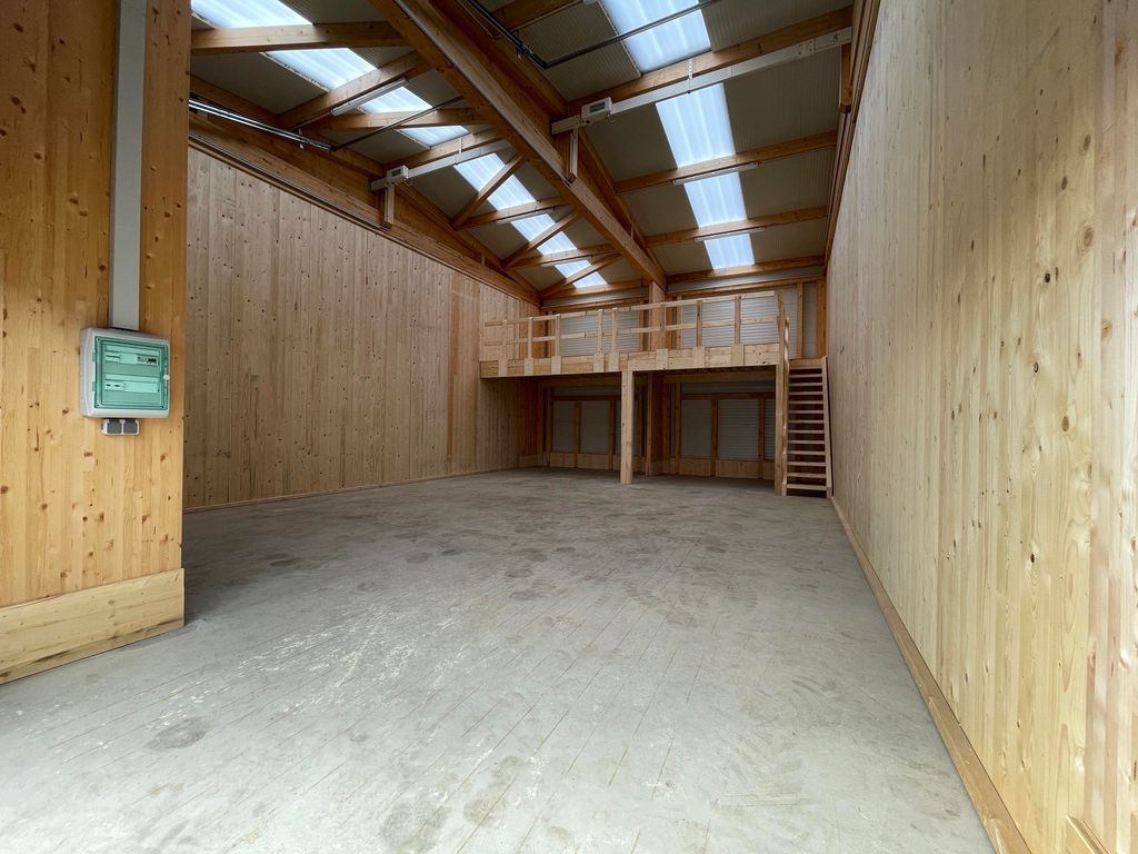 Leerer Lagerraum mit Holzwänden, Holzbalken an der Decke und einem erhöhten Bereich mit Treppe am Ende des Raums.