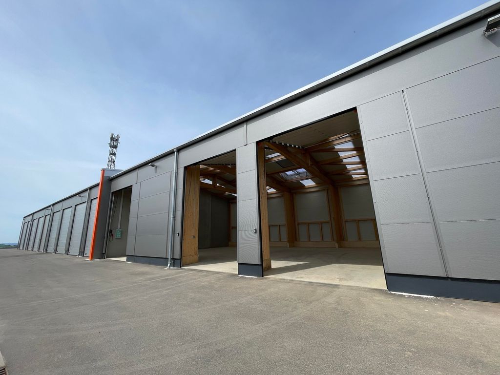 Große moderne Lagerhalle mit geöffneten Toren, grauen Außenwänden und sichtbaren Holzträgern im Inneren.