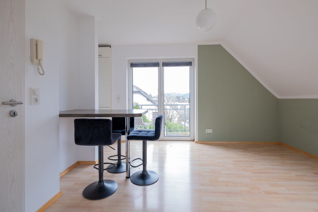 Ein heller, leerer Raum mit einem kleinen Esstisch und vier modernen Barhockern vor großen Glastüren mit Blick auf die Nachbarschaft.