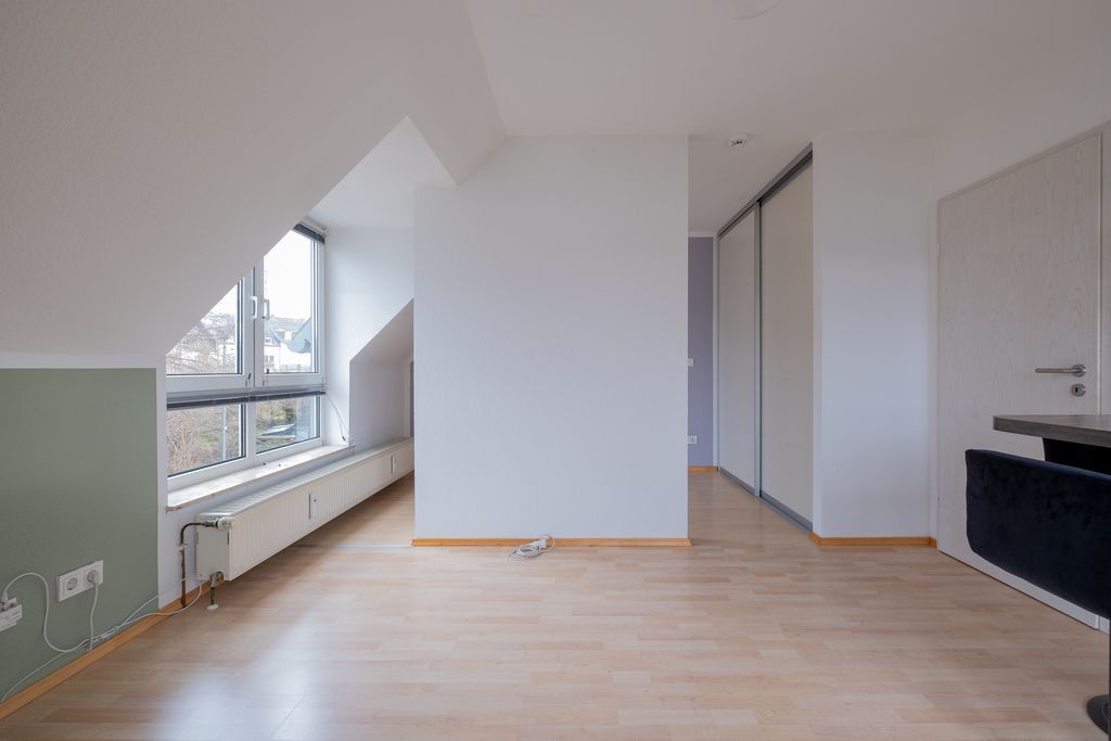 Leeres Zimmer mit hellen Holzböden, einer grünen Wand unten links, großen Fenstern und einer weißen Wand in der Mitte mit einem kleinen Objekt auf dem Boden.
