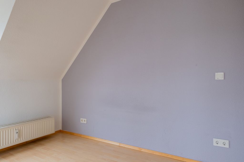 Leerer Raum mit hellvioletter Wand, weißer schräger Decke und Holzfußboden.