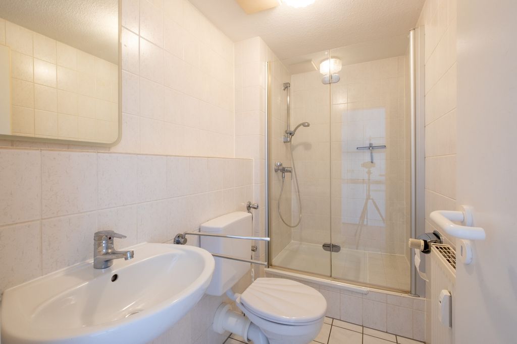 Helles Badezimmer mit einem Waschbecken, einer Toilette mit Haltegriff und einer Duschkabine mit Glastür.