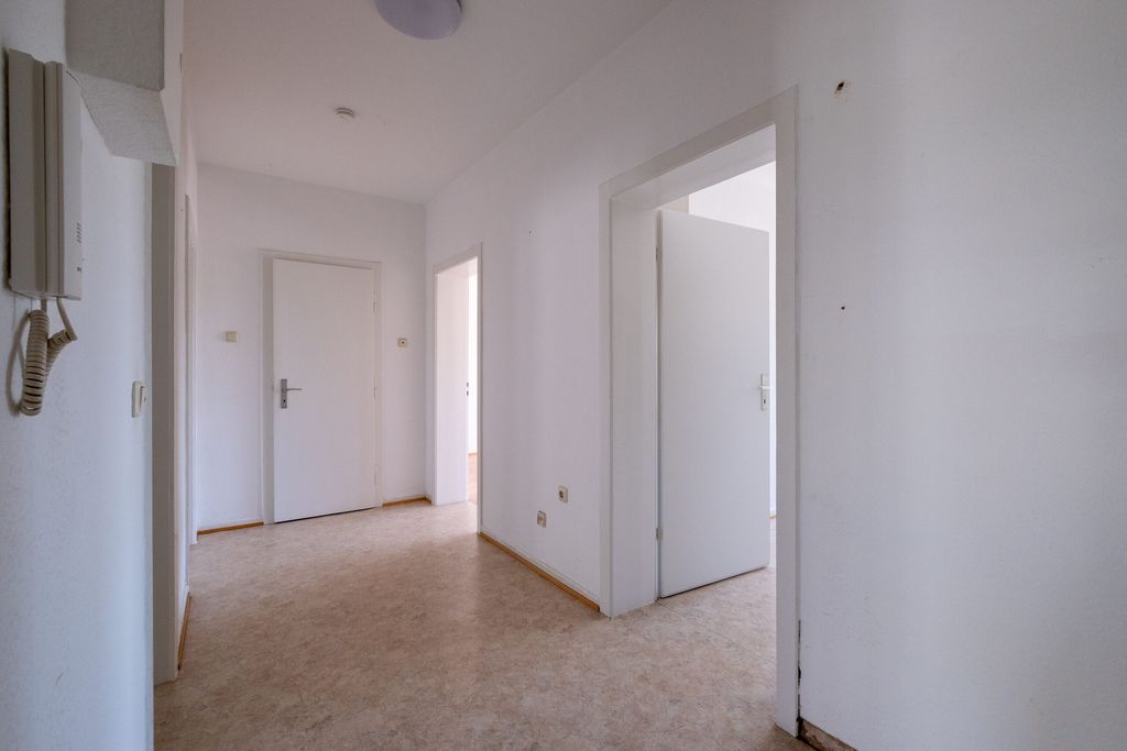 Leerer Flur mit weißen Wänden, mehreren geschlossenen und offenen Türen und einem hellen Bodenbelag.