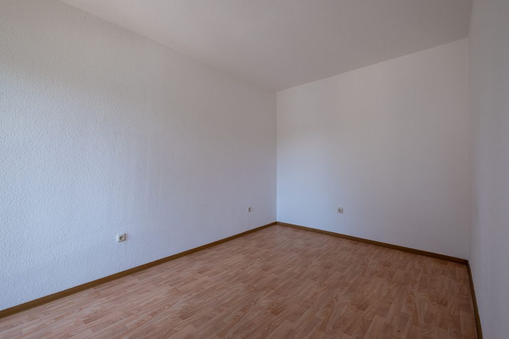 Leerer Raum mit weißen Wänden und hellem Holzfußboden, ohne Möbel oder Dekoration.