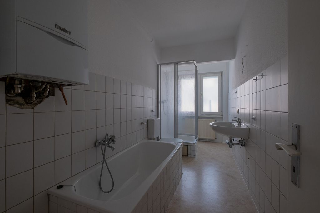 Kleines Badezimmer mit Badewanne, Duschkabine, Waschbecken und Heizkörper neben einem Fenster.