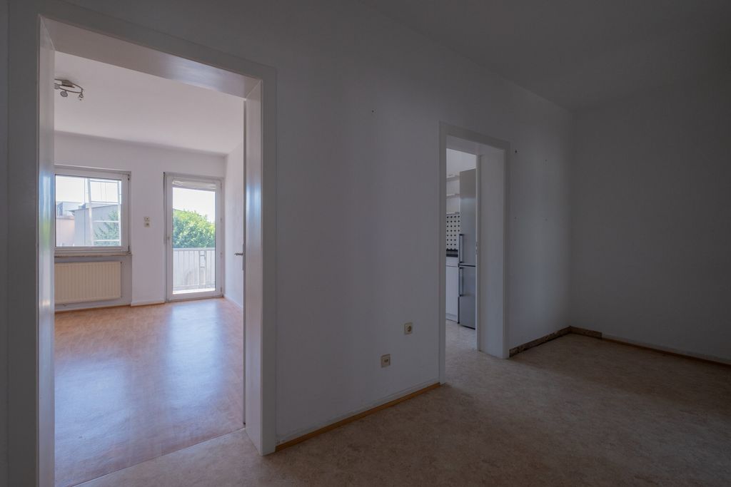 Blick in zwei nebeneinanderliegende, leere Räume eines Wohnraums mit weißen Wänden und einem Fenster sowie einer Terrassentür in einem Raum.