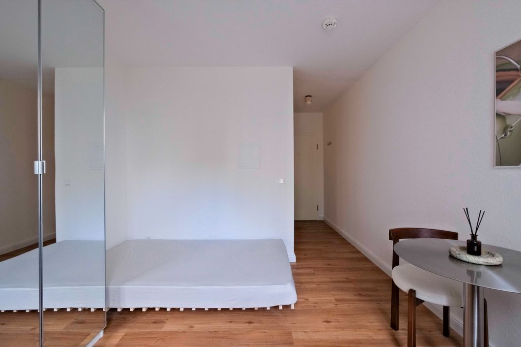 Minimalistisches Schlafzimmer mit einem niedrigen Bett ohne Rahmen und einem kleinen runden Tisch mit zwei Stühlen auf Holzboden.