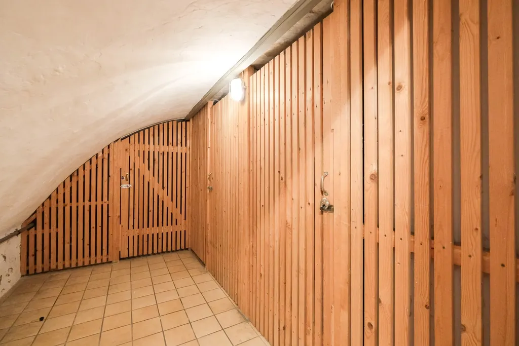 Flur mit geneigter Decke und verschlossenen Holzlattentüren, beleuchtet von einer Deckenlampe.