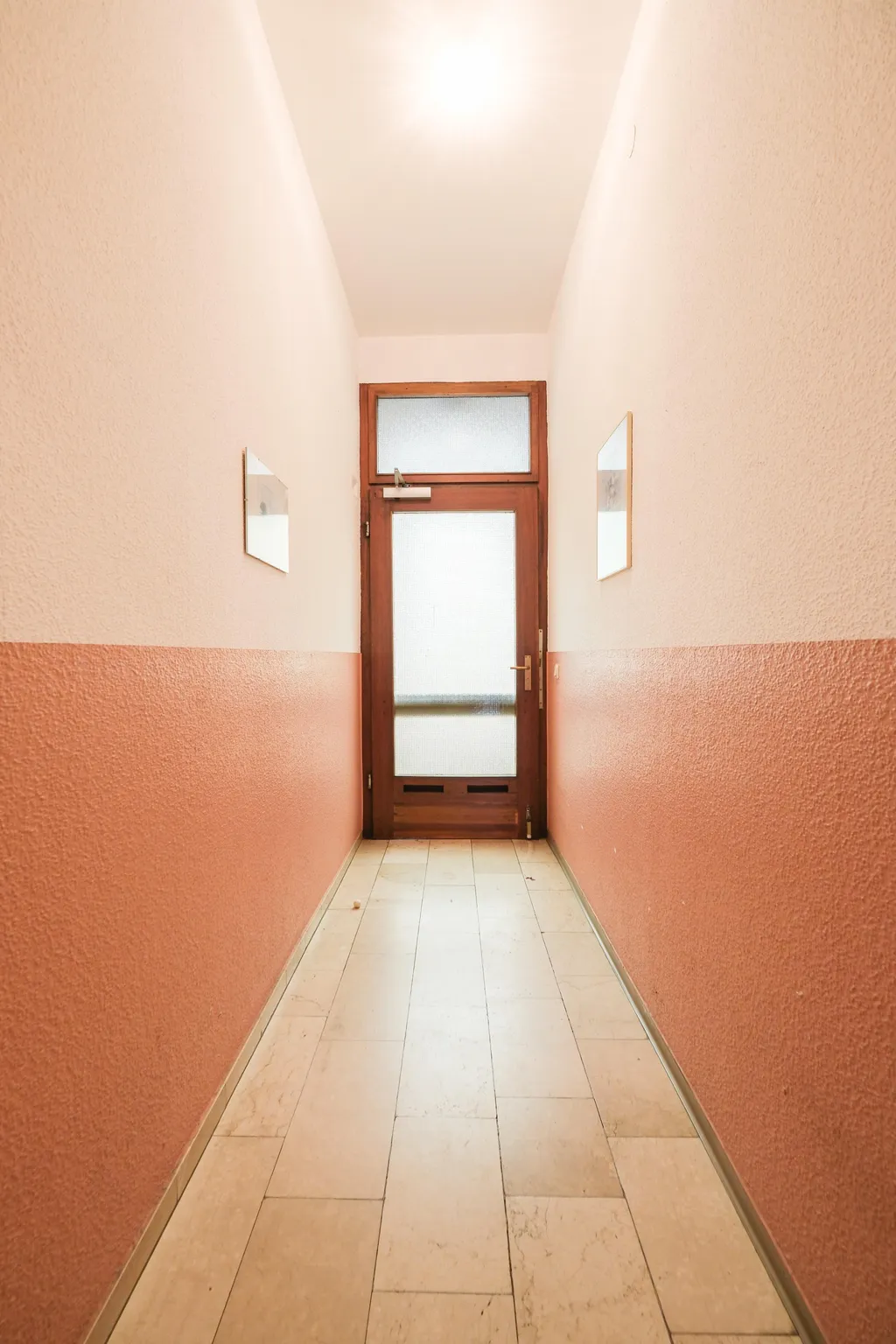 Schmaler Flur mit halbhohen roten Wänden und einer Tür mit Fenster am Ende.