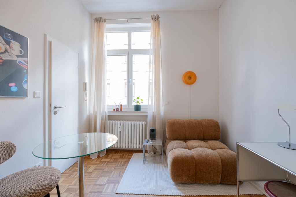 Helles Wohnzimmer mit einem großen Fenster, braunem, modernen Sofa, einem Glas-Ecktisch und einem weißen Teppich auf dem Holzparkettboden.